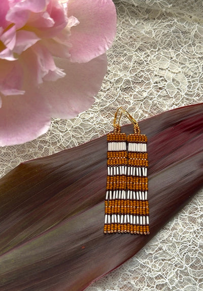 Beaded earrings with vertical stripes on a textured surface with a pink flower in the background